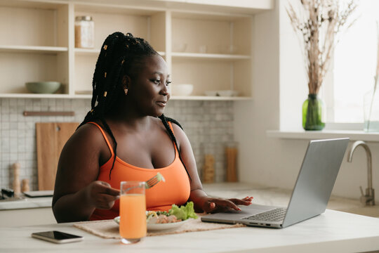 Beautiful Plus Size African Woman Working On Laptop While Enjoying Healthy Eating For Lunch At Home