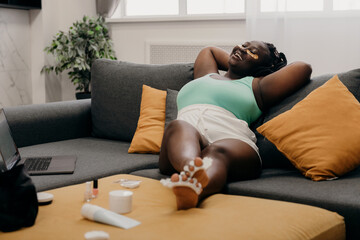 Happy plus size African woman with eye patches on face enjoying spa day at home