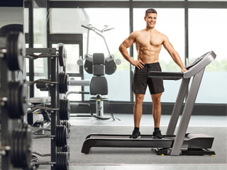 Fototapeta na wymiar Full length shot of a bodybuilder posing on a treadmill at the gym