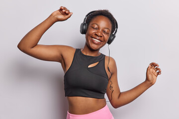 Horizontal shot of African dressed in cropped top and pink leggings enjoys listening music via...
