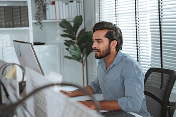 Young serious indian professional business man working with computer at home office, businessman at...