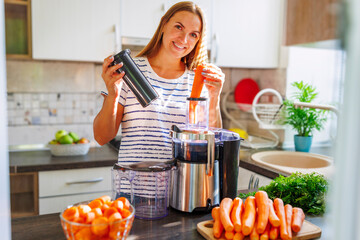 A woman making carrot juice from fresh carrots with a home juicer in the kitchen
