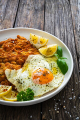 Crispy breaded seared chicken cutlet with fried egg on and  lemon on wooden table
