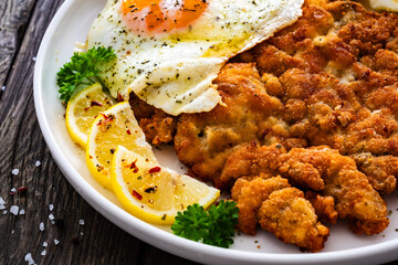 Crispy breaded seared chicken cutlet with fried egg on and  lemon on wooden table

