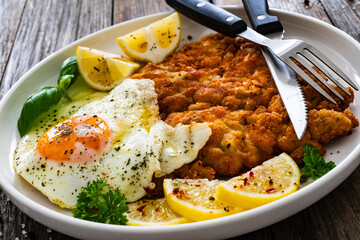 Crispy breaded seared chicken cutlet with fried egg on and  lemon on wooden table
