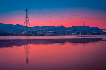 Fototapeta na wymiar Daegu City sunset landscape at Gangjeong-Goryeong Weir or Dam with electricity pylons, power lines and mountains reflected on the Nakdong River, South Korea