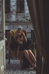 Lady in peignoir with a glass of wine. Sensual photo of European Blonde woman in black silk robe with feathers sleeve. Fashionable concept