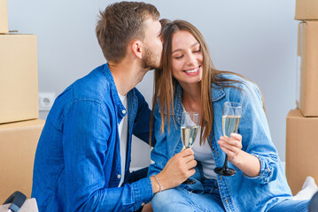 Couple taking a break on moving day, sitting on floor in new apartment celebrating with champagne...