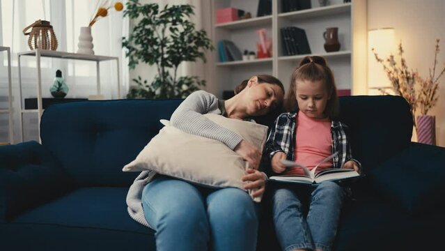 Tired mom sleeping while little daughter is reading, challenges of parenting