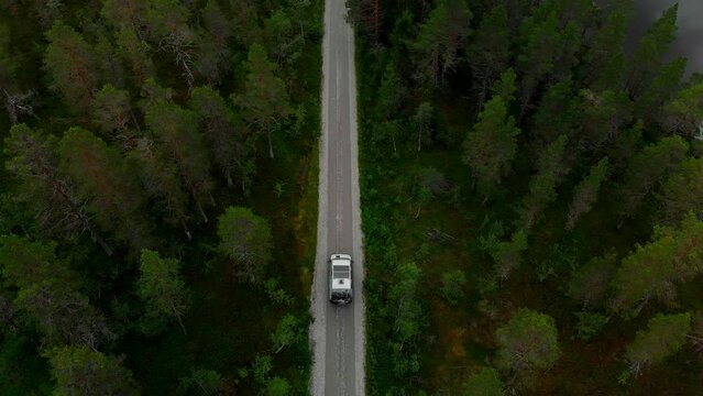 Aerial top down view on off-grid camper van with solar panels system on roof drive on gravel dirt road in the forest. Vanlife adventure concept