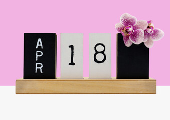 Secretary's day on April 18. Wooden calendar with date and Phalaenopsis flower, isolated on pink background. Greeting card .