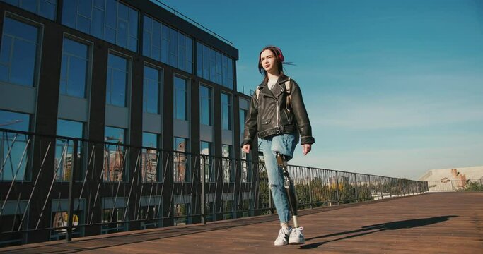Young woman student with prosthetic leg walking in university campus. Woman with bionic leg. Woman with leg prosthesis equipment
