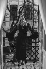 Lady in peignoir with a glass of wine. Sensual photo of European Blonde woman in black silk robe with feathers sleeve. Fashionable concept