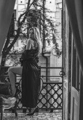 Fototapeta na wymiar Lady in peignoir with a glass of wine. Sensual photo of European Blonde woman in black silk robe with feathers sleeve. Fashionable concept