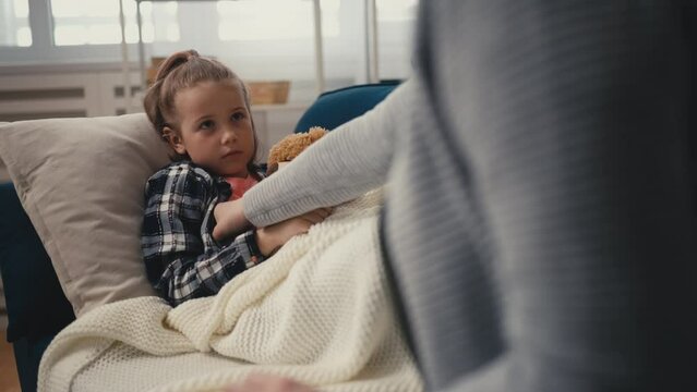 Mother taking care of ill child on couch, taking temperature, touching forehead