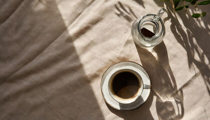 elegant minimalist morning concept cup of coffee glass vase and aesthetic sunlight shadows on neutral beige table cloth top view flat lay