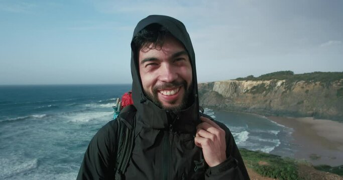 Portrait of hispanic young man look at camera and laugh. Cinematic shot of male hiker in windproof jacket with hood laugh and smile. Authentic emotions out in the nature