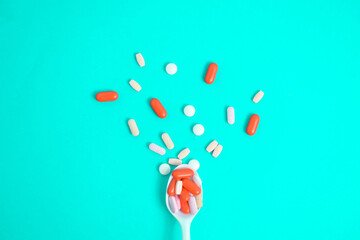 Colorful Medicine Pills in White spoon on green tosca background, supplement, vitamin, colorful