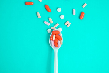 Colorful Medicine Pills in White spoon on green tosca background, supplement, vitamin, colorful