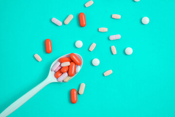 Colorful Medicine Pills in White spoon on green tosca background, supplement, vitamin, colorful
