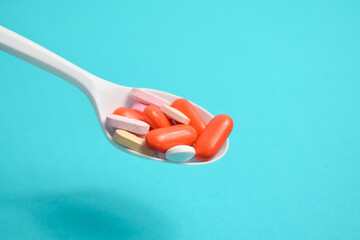 Colorful Medicine Pills in White spoon on green tosca background, supplement, vitamin, colorful