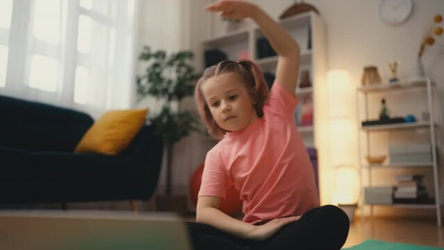 Cute child doing exercise at home, watching tutorial on laptop, motivation