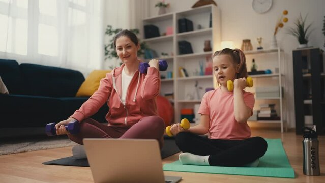 Mom and daughter lifting dumbbells together, watching online tutorial on laptop