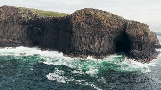 Aerial view flying over a Fingal's Cave on Staffa Island, west of Isle of Mull in Scotland. Calm waves touching the rocks. 4k video.