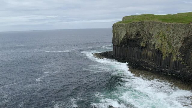 Aerial view flying over a Fingal's Cave on Staffa Island, west of Isle of Mull in Scotland. Calm waves touching the rocks.