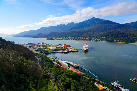 Aerial view of the Gastineau Channel, a fjord in the North Pacific leading to Juneau, Alaska's Capital City - Cruise ship moored to a pier surrounded by mountains covered with pine forests