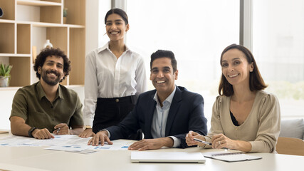Positive successful multiethnic business team office portrait. Happy Indian, Arab, Latin colleagues sitting at meeting table together, looking at camera, smiling, laughing