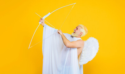 Valentines Day celebration. Arrow of love. Smiling blonde man in angel costume shooting love arrow. Valentine angel with white wings shoots love arrow from bow. Cupid with bow and arrows. God of love.