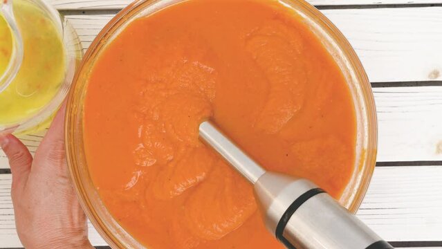 Roasted butternut squash soup recipe, preparation process. Blending roasted vegetables into a puree, adding vegetable stock in a bowl, close-up view