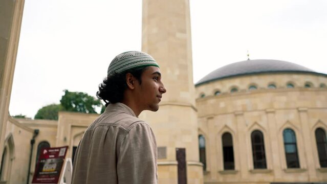 Back shot of a young Arab man entering the inner courtyard of a mosque on terrace with Islamic ornamentation 