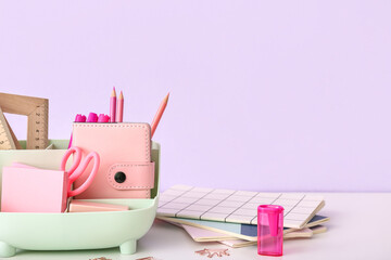 Holder with different stationery and notebooks on light desk, closeup