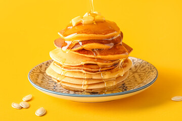 Plate of tasty pumpkin pancakes with honey on yellow background
