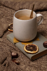 Cozy winter lifestyle concept. Cup of hot drink with vintage book and warm knitted clothes.	