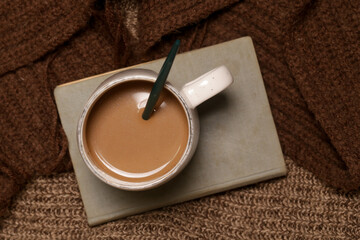 Cozy winter lifestyle concept. Cup of hot drink with vintage book and warm knitted clothes.