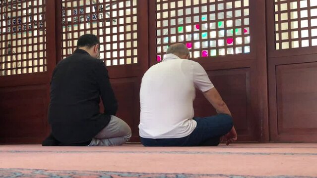 2 men with their backs turned as they sit for prayer in a mosque in Istanbul