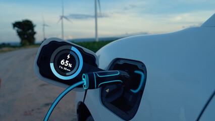 Electric car recharging energy from EV charging station display futuristic smart battery status hologram by EV charger plug cable in wind turbine farm. Alternative clean energy sustainability. Peruse