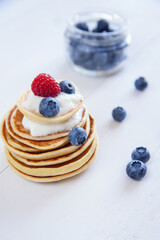 Delicious homemade pancakes with yogurt and fresh blueberries on white wooden background.