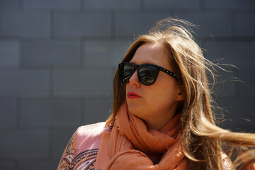 Portrait of mid 30 business woman with waving brown hair with black sunglasses smiling and gray...