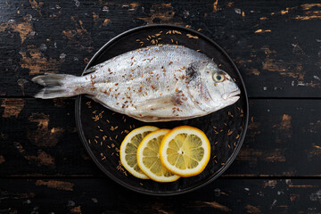 Raw dorado fish with lemon and cumin seeds on black plate. Top view