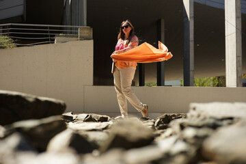 Cool confident woman with sunglasses in orange fashion clothes waving orange scarf in business...