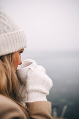 Young pretty woman holding cup of tea enjoying winter frozen nature by the sea