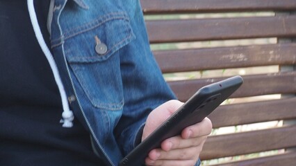 smiling happy fun teenage schoolboy boy sits in a park on a bench use mobile cell phone chat online rest relax outdoors Urban. spending time on social networks, online training, conference. video call