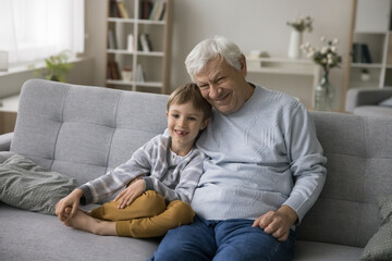 Old great-grandpa hugs his cute little great-grandson smile look at camera posing for family photo, spend leisure at home together, having good harmonic. Relationships feeling love, express affection