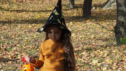 happy laughing child girl in witch costume to halloween. with a jack-o'-lantern candy bowl, trick...