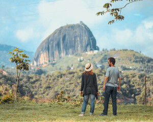 casal de costas lado a lado diante de pedra ao fundo, em Guatapé, Colombia  - obrazy, fototapety, plakaty
