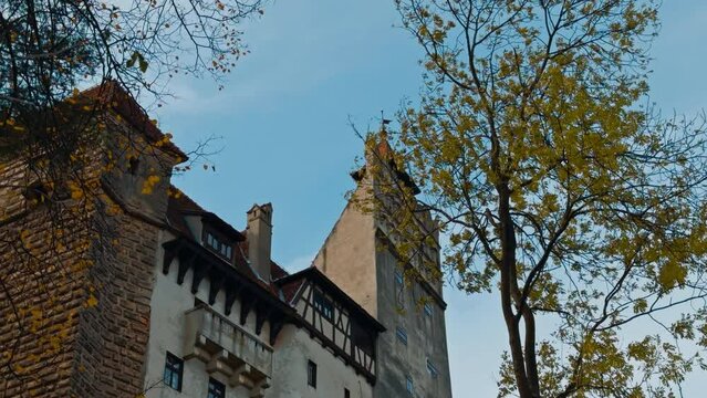 Beautiful fasade of Bran castle in Romania. Low angle view on the building and trees with little foliage.